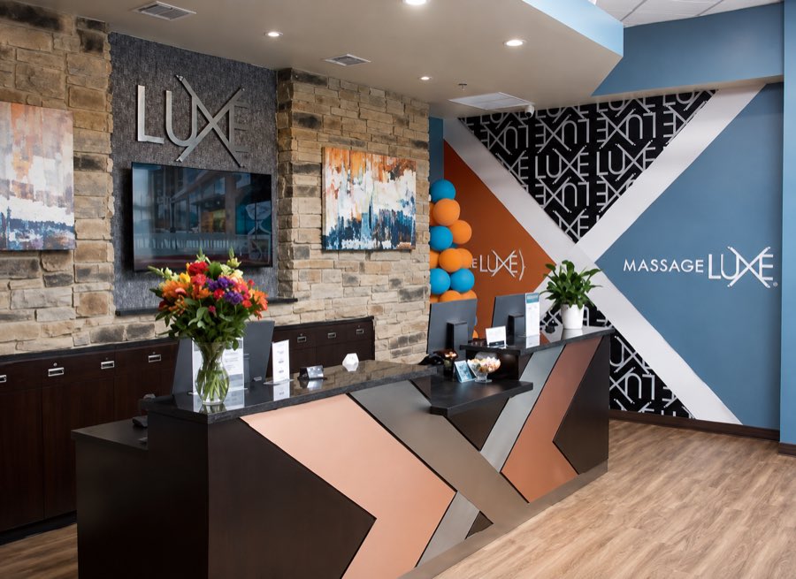 MassageLuXe reception with a stone feature wall, custom desk and graphic wall treatment