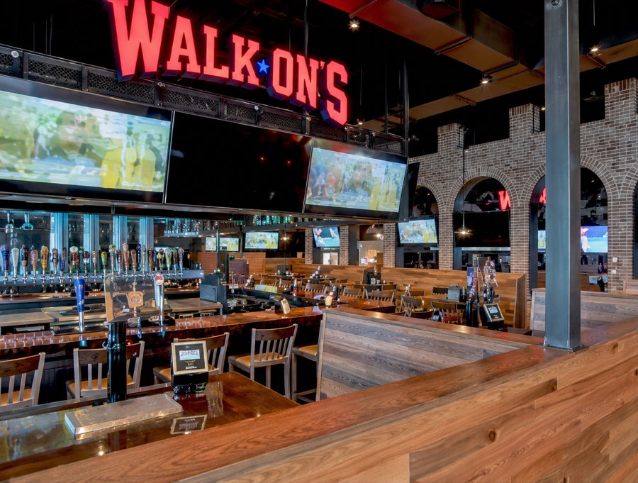 Interior bar and dining room at Walk-On&rsquo;s Sports, with exposed steel, brick archways and a full-length bar